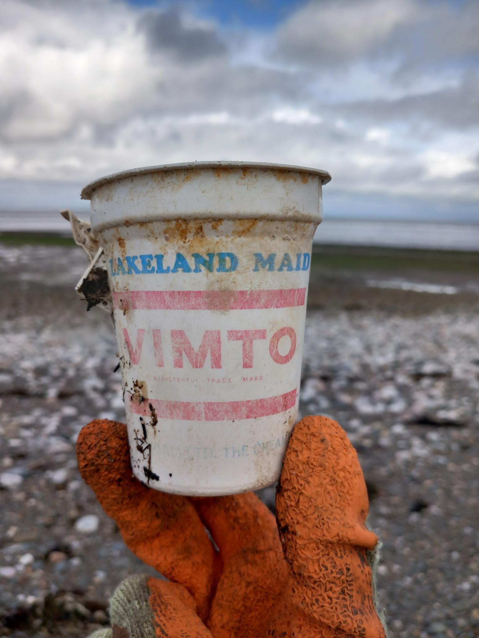 a gloved hand holding an old Vimto container